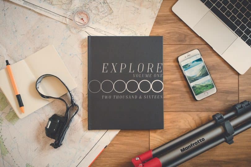 Explore Book Beside Silver Iphone 6 on Brown Wooden Surface