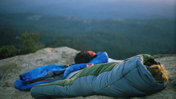 photo of a woman in a sleeping bag on the top of the mountains