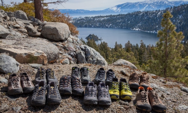 A lot of pair of hiking boots and a landscape in the background