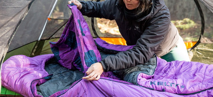a camper carefully using their sleeping bag zipper