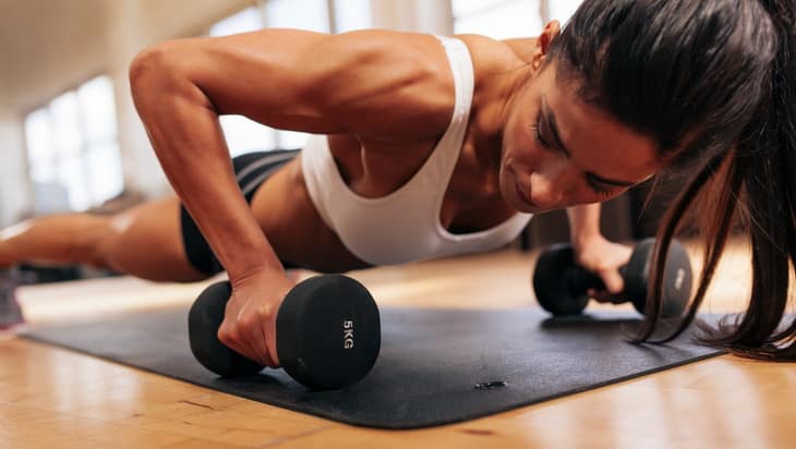 Strong young woman doing push ups exercise with dumbbells