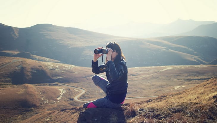 Woman Wearing Black Jacket Using Binoculars Sitting on Mountain