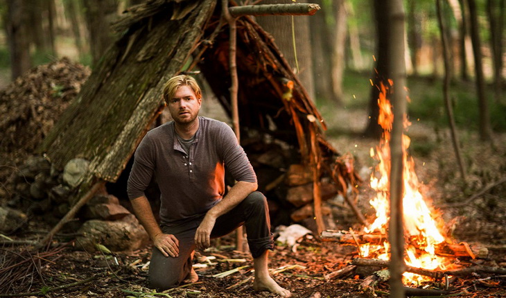 A man in the wild near a fire looking at the camera