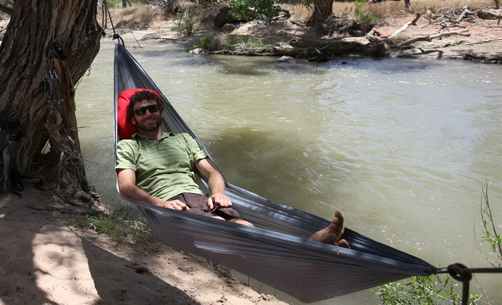 A man in Grand Trunk Nano 7 Hammock near a river