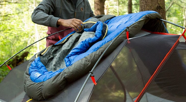 A man drying his sleeping bag on a tent