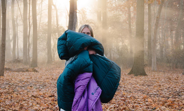 A woman in the forest holding Kelty sleeping bag