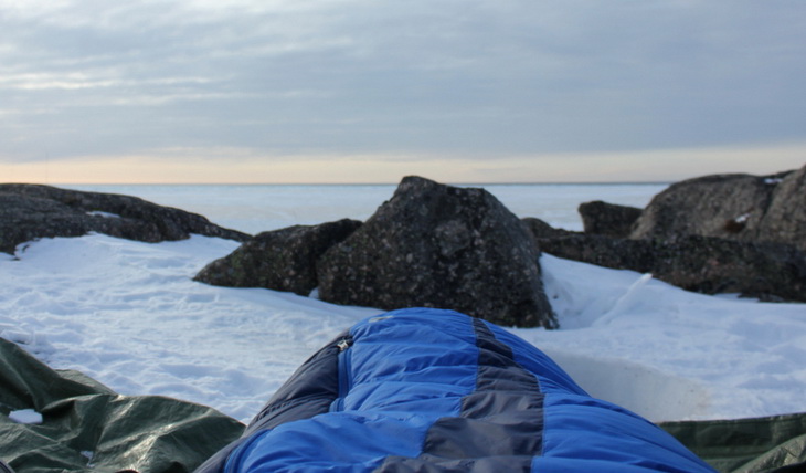 Image of a person sitting in a sleeping bag outside in the winter time