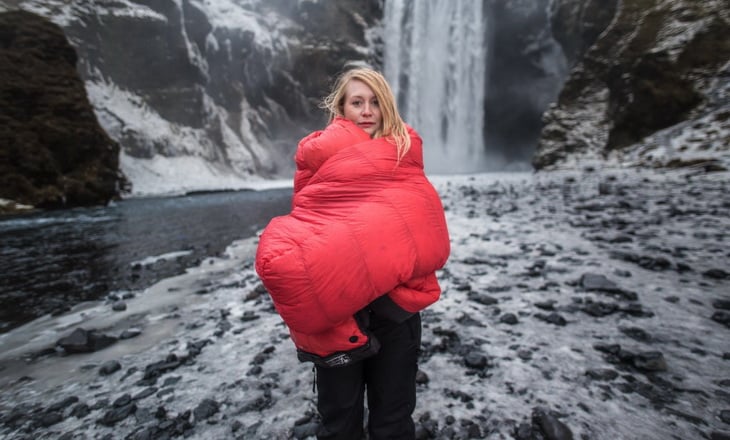 Woman with a sleeping bag in front of a waterfall