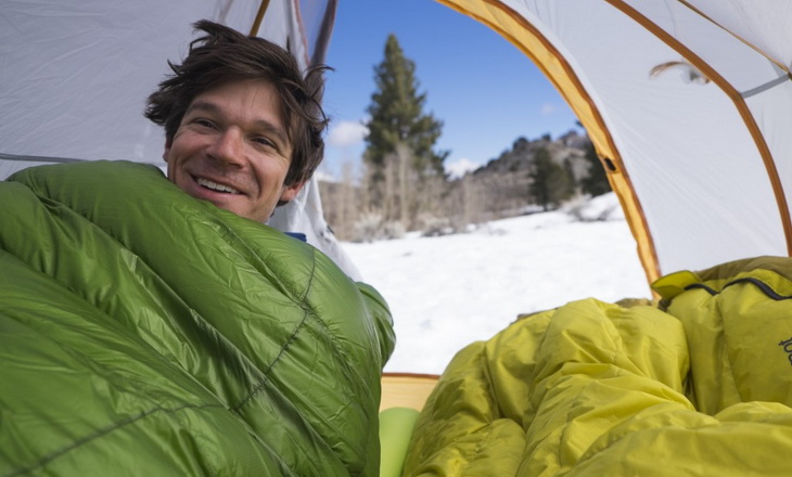 Man sitting in a Down Sleeping Bag smiling at the camera