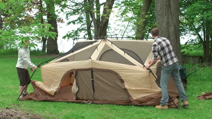 Two persons setting up a tent in the forest
