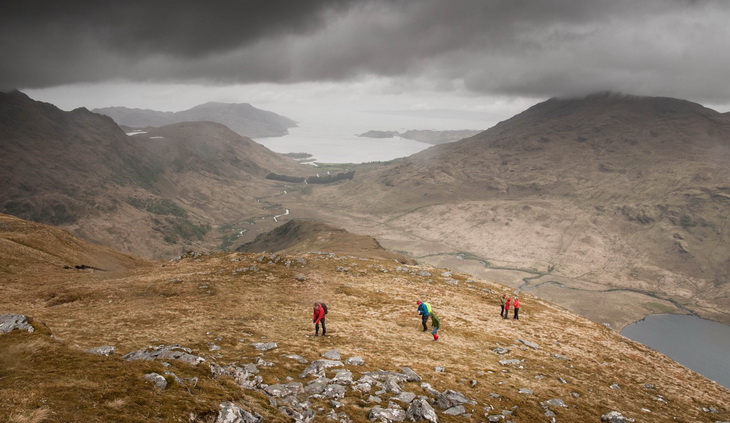 People Standing on Brown Mountain Near Lake Under Gray Clouds during Day Time