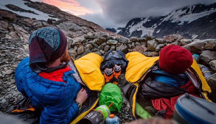 Two adults sitting in sleeping bags looking at the moutains