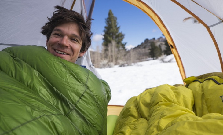 Man in a sleeping bag in tent smiling at the camera