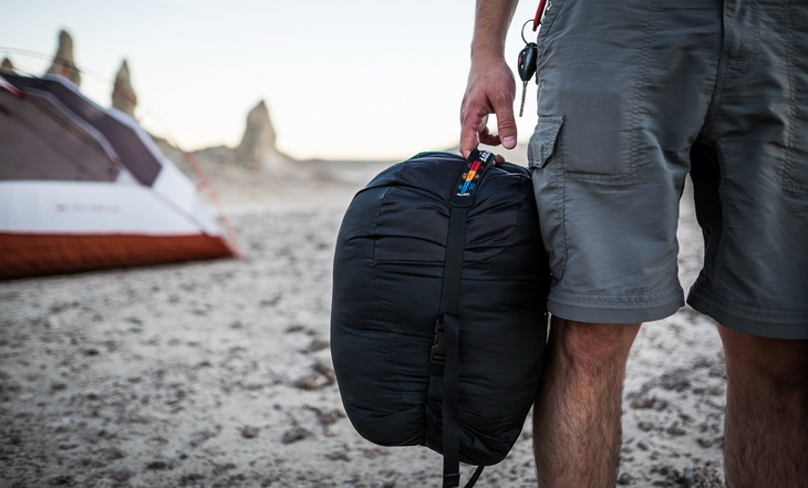 Man on a beach holding The North Face Cat's Meow Sleeping Bag