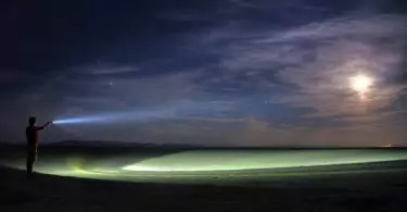 guy holding a LED flashlight over the lake