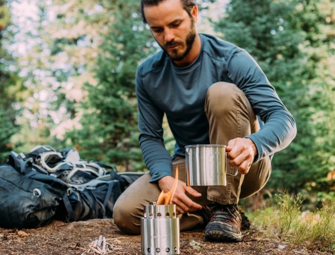 man firing backpacking stove on ground