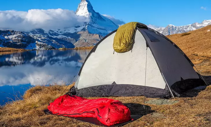 One sleeping bag on a tent and one on the ground and a mountains landscape