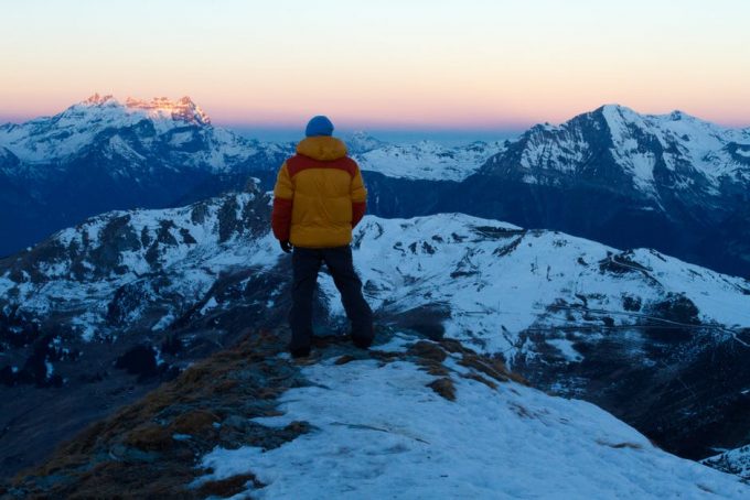 A hiker with yellow-red jacket on a snowy hilltop