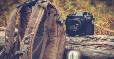 An outdoorretro photo camera next to a backpack and a thermos