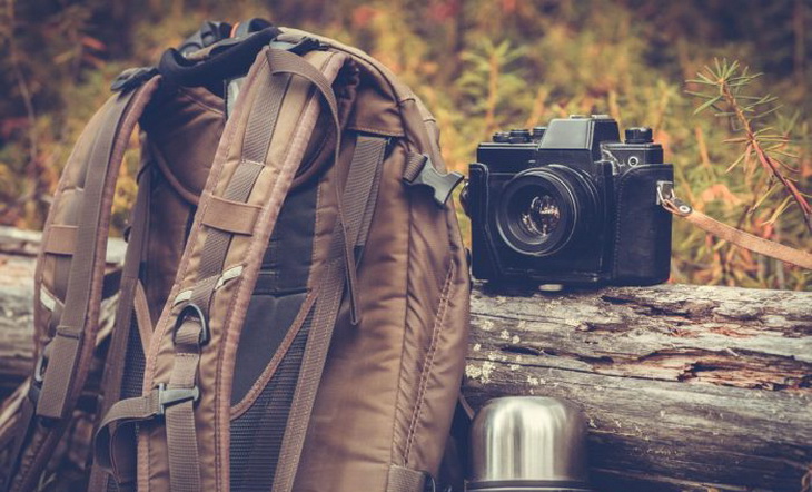 An outdoorretro photo camera next to a backpack and a thermos