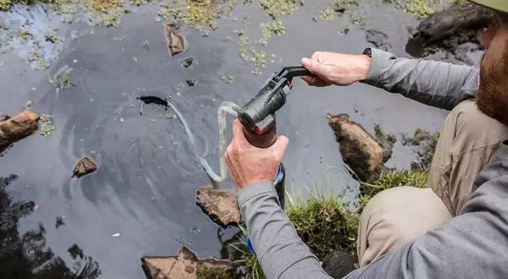 A man filtering the water using a backpacking water filter