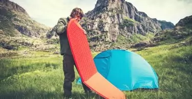 Man Traveler holding red mattress camping equipment and tent outdoor Travel Lifestyle concept rocky mountains landscape on background Summer adventure vacations