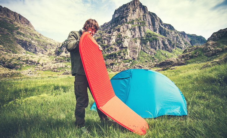 Man Traveler holding red mattress camping equipment and tent outdoor Travel Lifestyle concept rocky mountains landscape on background Summer adventure vacations