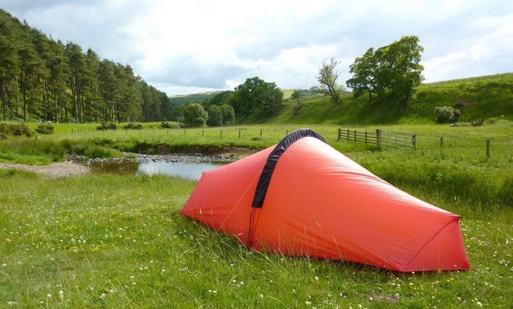 A red solo tent in the summer time and a nature landscape