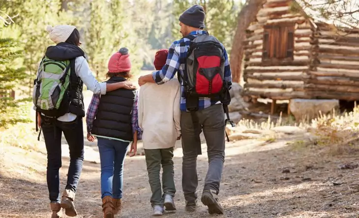 Two aduls wearing daypack hiking with their childrens