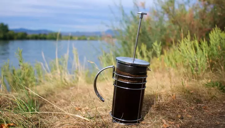 French Press Coffee Maker on the grass near a water