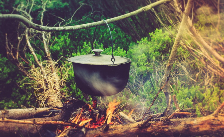 A person cooking on a campfire in the summer time