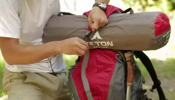 A man fixing a tent to a backpack