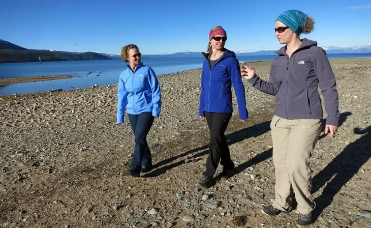 Three womens wearing softshell jackets hiking near a water