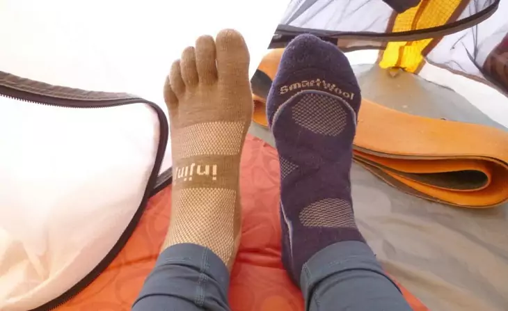 A person is testing two different type of warm socks in a tent