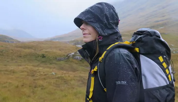 A woman wearing a waterproof jacket is hiking on the mountains