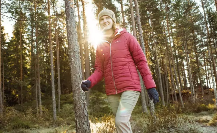 Woman wearing a red parka jacket is hiking in the forest