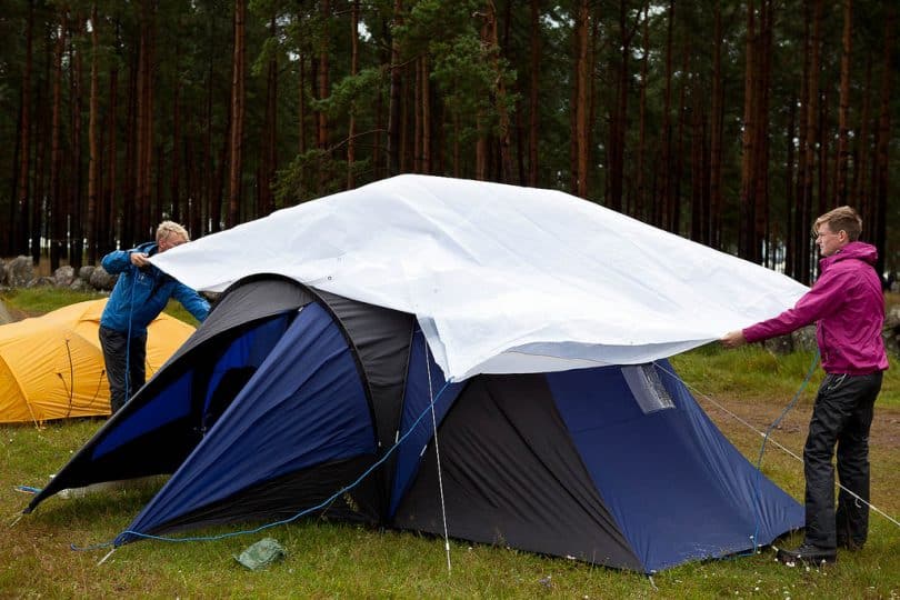 Zwei Erwachsene, die ein undichtes Zelt mit einer Plane abdecken, um den Regen fernzuhalten