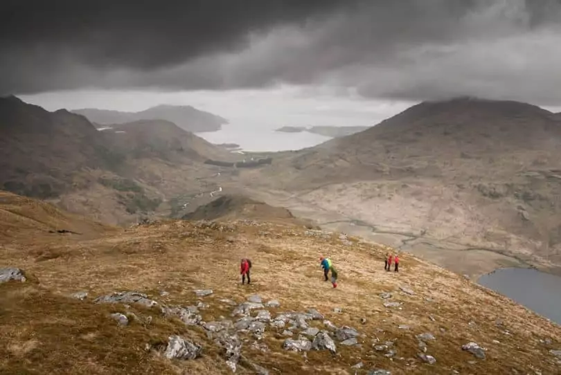 People Standing on Brown Mountain Near Lake Under Gray Clouds during Day Time