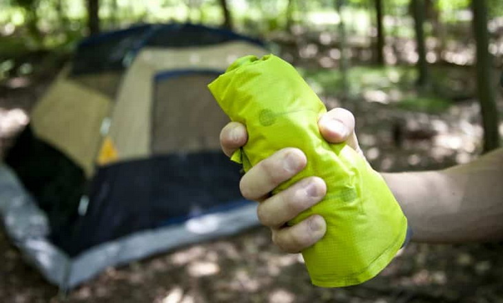 A man holding a sleeping pad in his hands and a tent in the background