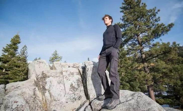 A men wearing a base layer sitting on a rock and looking at the landscape