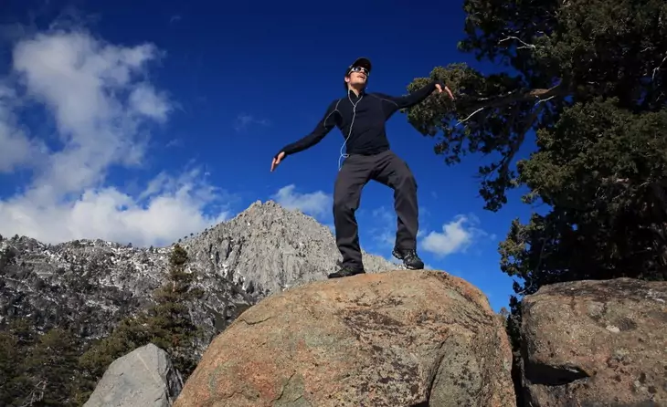 A man wearing a base layer dancing on a rock on top of the moutains