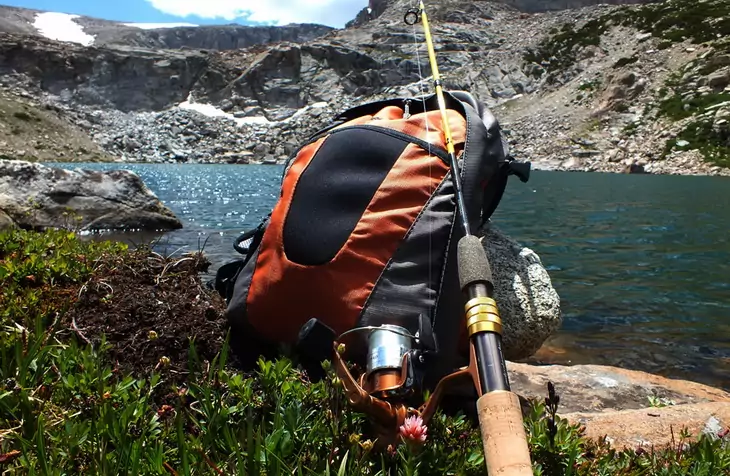 A fishing rod sitting on a backpack and a lake landscape