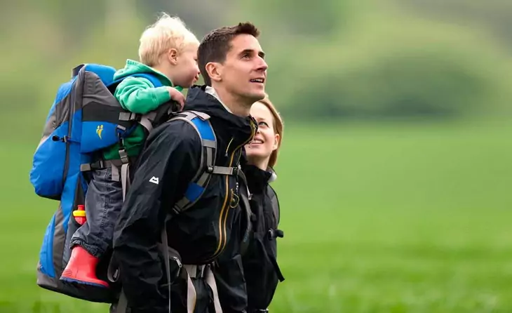 A toddler carried by his father in a backpack