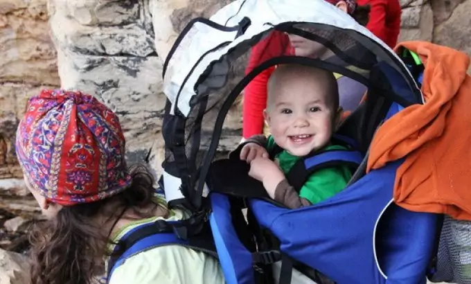 picture of a child in a baby carrier smiling at the camera