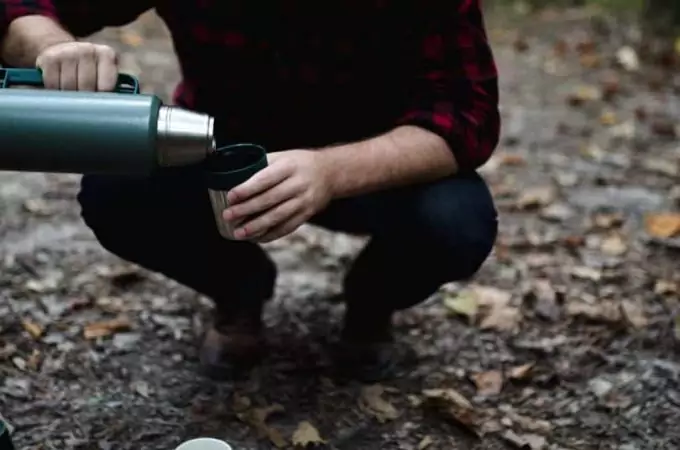 A man pouring some coffee in a cup of a camping thermos