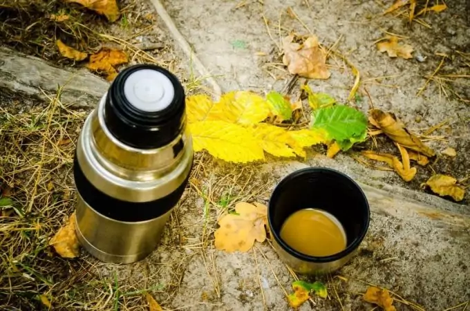 A camping thermos and a cup of coffee on the ground