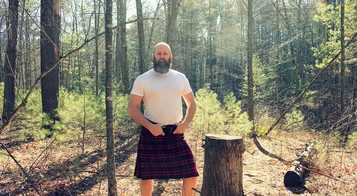 A man with a beard is wearing a kilt in the forest