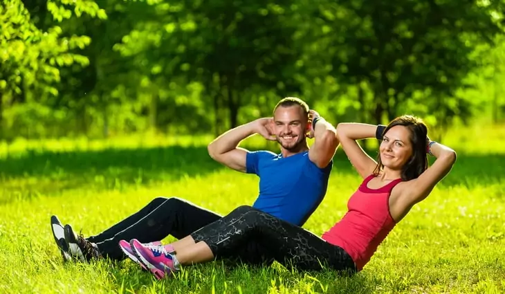 two adults doing sit ups exercises outside on the grass
