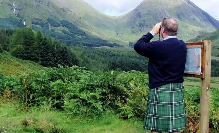 A man with a kilt is looking at the moutains landscape