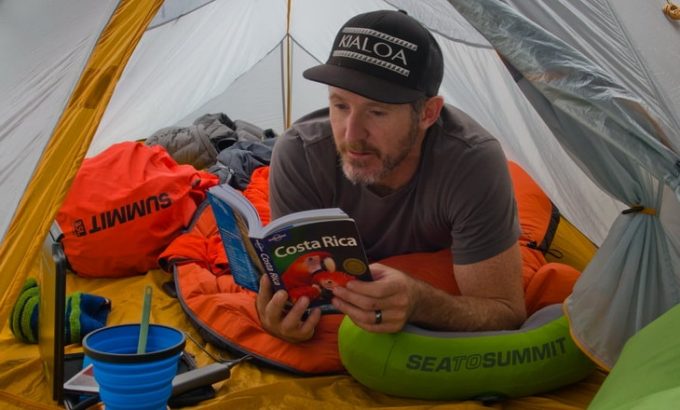 A-man-sitting-in-a-sea-to-summit-sleeping-bag-liner-and-reading-a-book